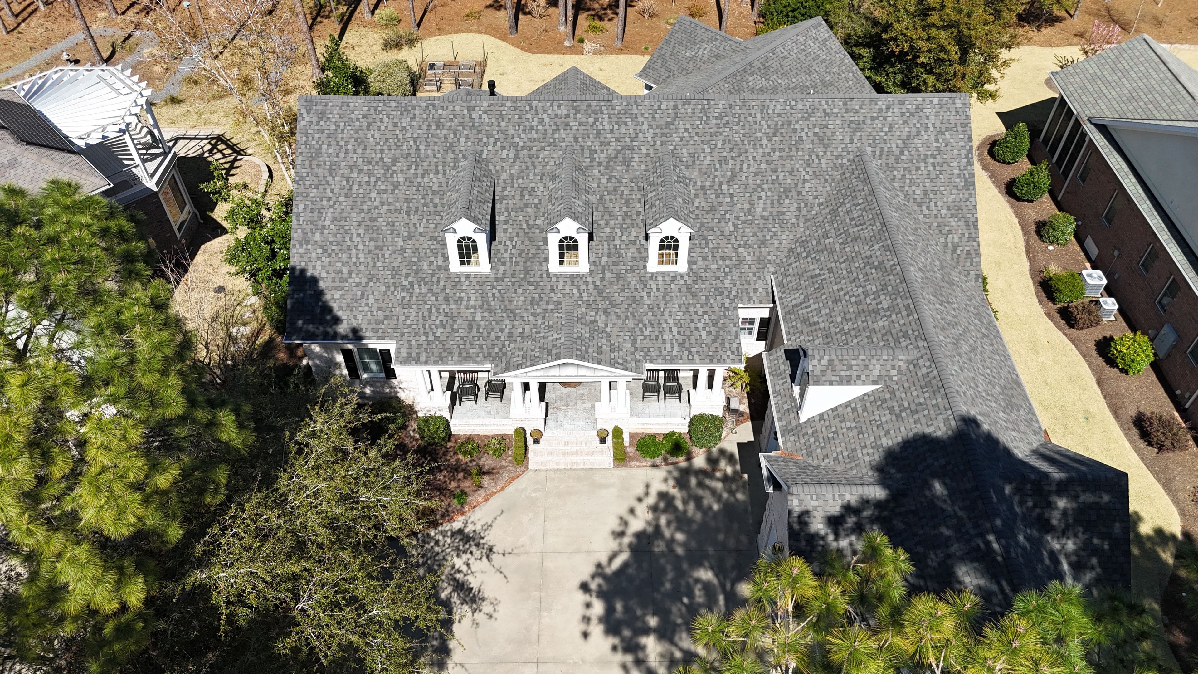Aerial view of a large, elegant house with a gray roof and landscaped yard.