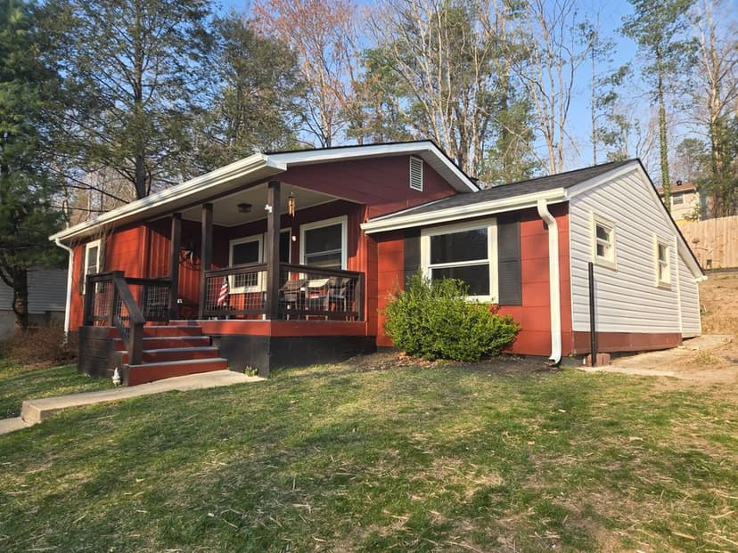 Charming red and gray house with a porch, surrounded by greenery and trees.