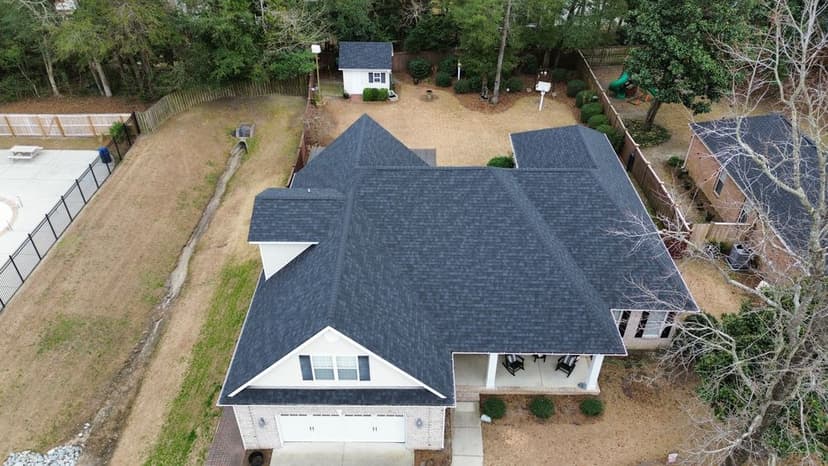 Aerial view of a residential home with a dark roof and surrounding yard features.